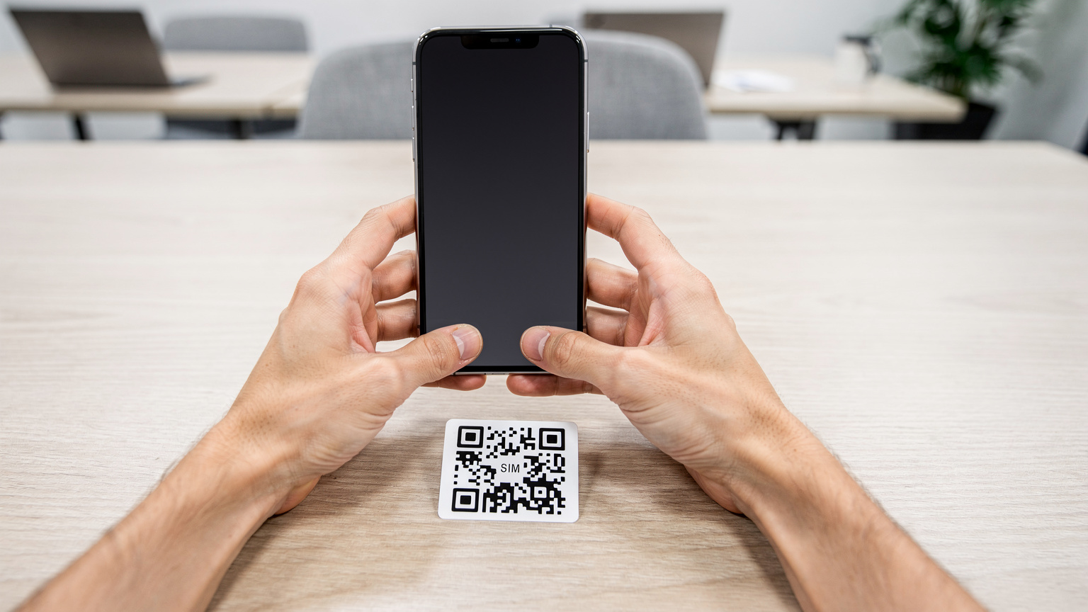 Close-up of human hands using a smartphone to scan an eSIM QR code, showing the simplicity of activation in a modern, clean setting.