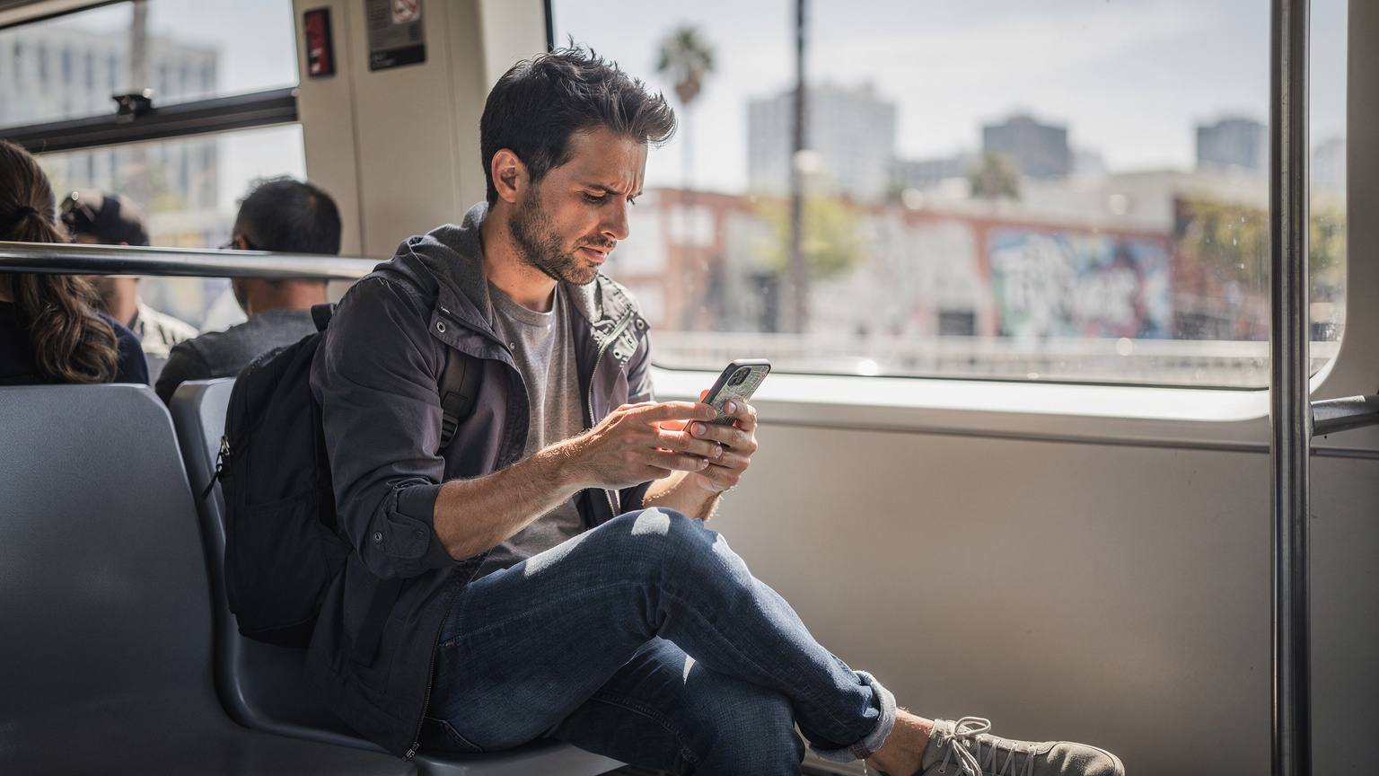Ein Reisender im Los Angeles Metro Rail, der auf seinem Smartphone eine Offline-Karte der Stadt studiert, während im Hintergrund durch das Fenster die Stadtkulisse vorbeizieht.