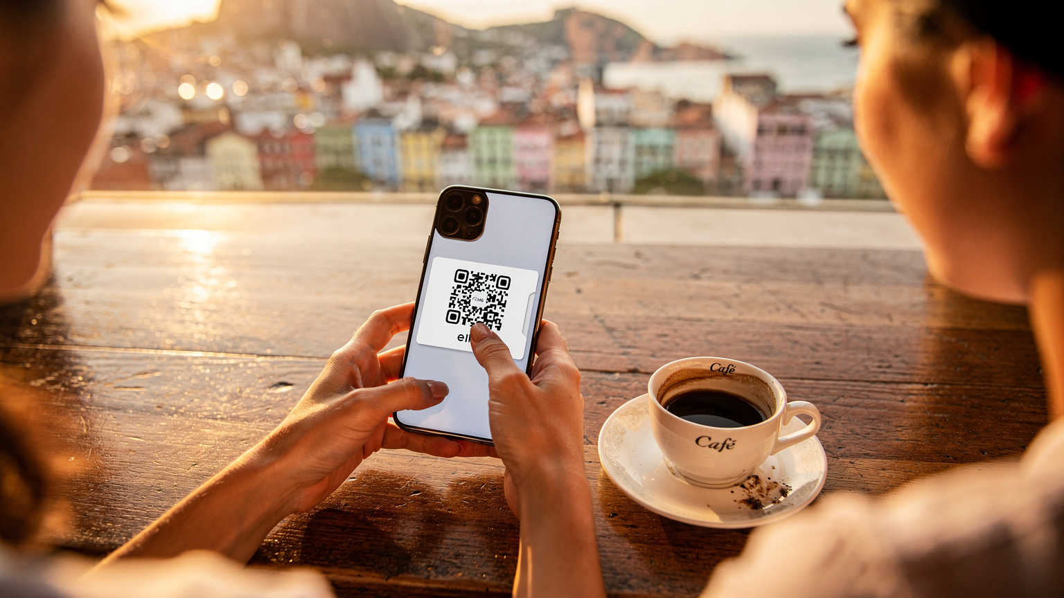 Bir kafede kahve içerken telefonunda eSIM QR kodunu tarayan bir gezginin elleri, arkada Rio manzarası.
