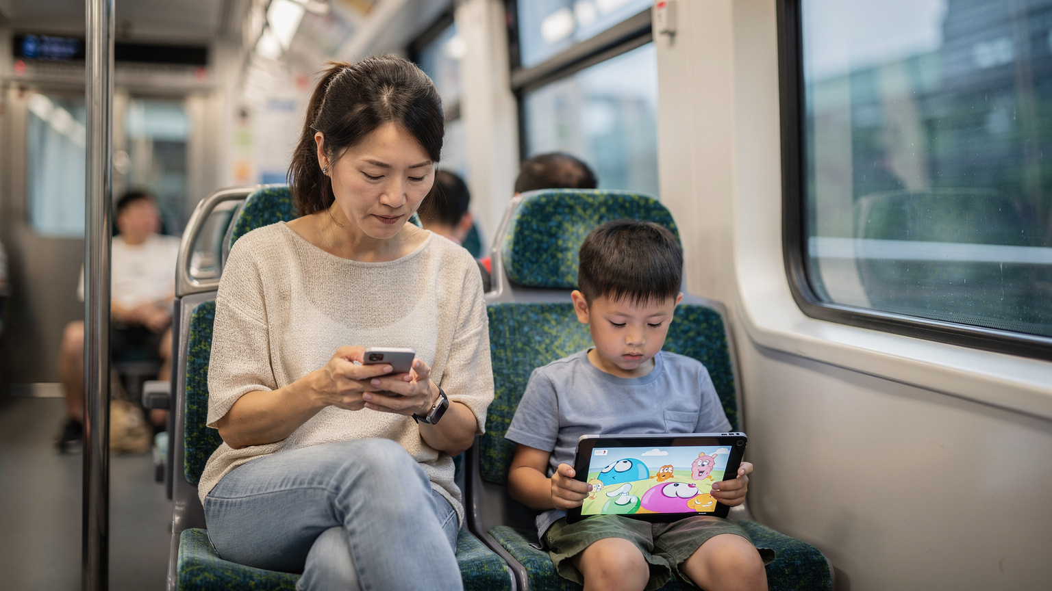 一位母亲在香港的地铁车厢内, 她的孩子正专注地看着iPad。母亲的手机显示她正在查看eSIM数据使用情况。