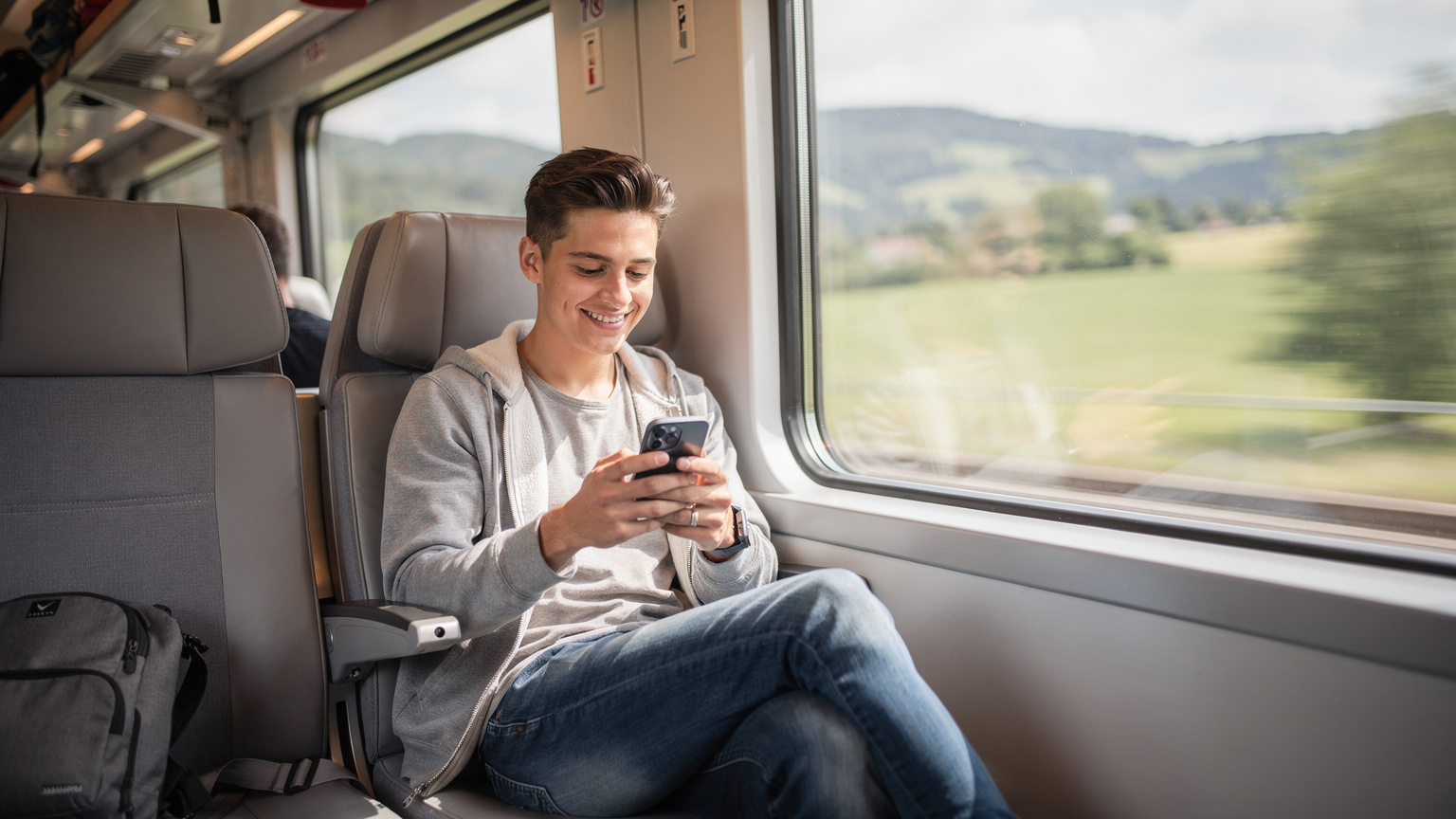 Un voyageur consulte son téléphone dans un wagon de train européen moderne, profitant de la connectivité en mouvement.